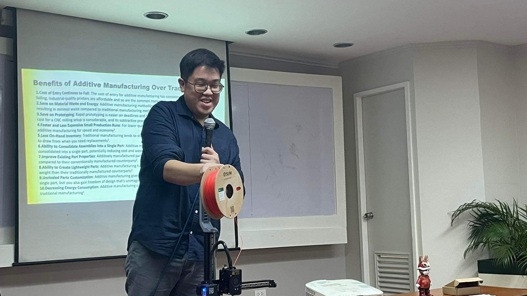 Charles Lu demonstrating a filament spool beside a live desktop 3D printer during the UE additive manufacturing workshop